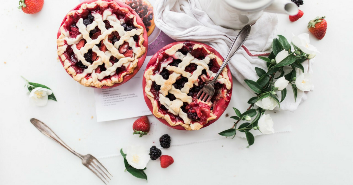 Berry pies, fork in partially eaten pie, loose berries, printed paper, cloth, greenery and flowers.