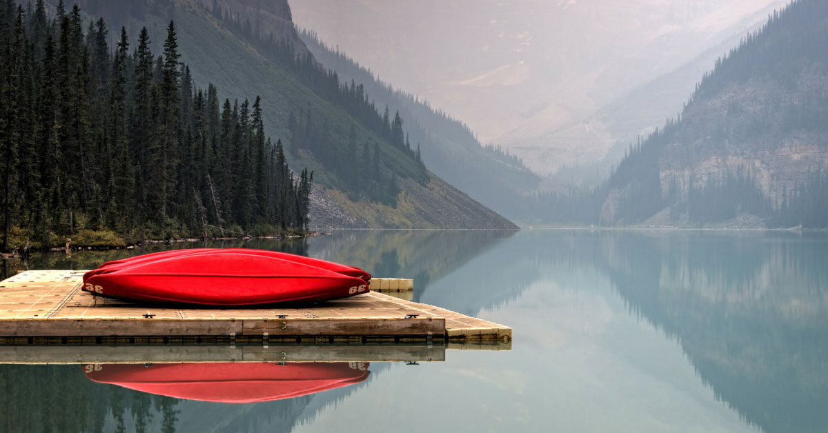 Canoe on dock at lake with mountain behind.