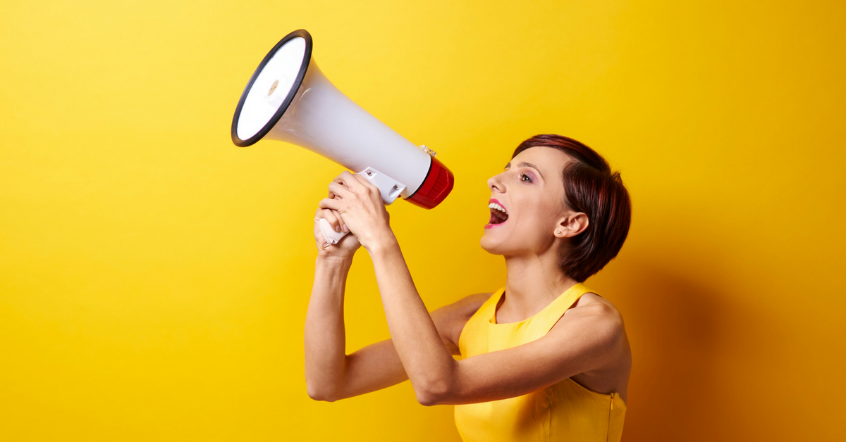 Woman in yellow dress speaking into a megaphone.