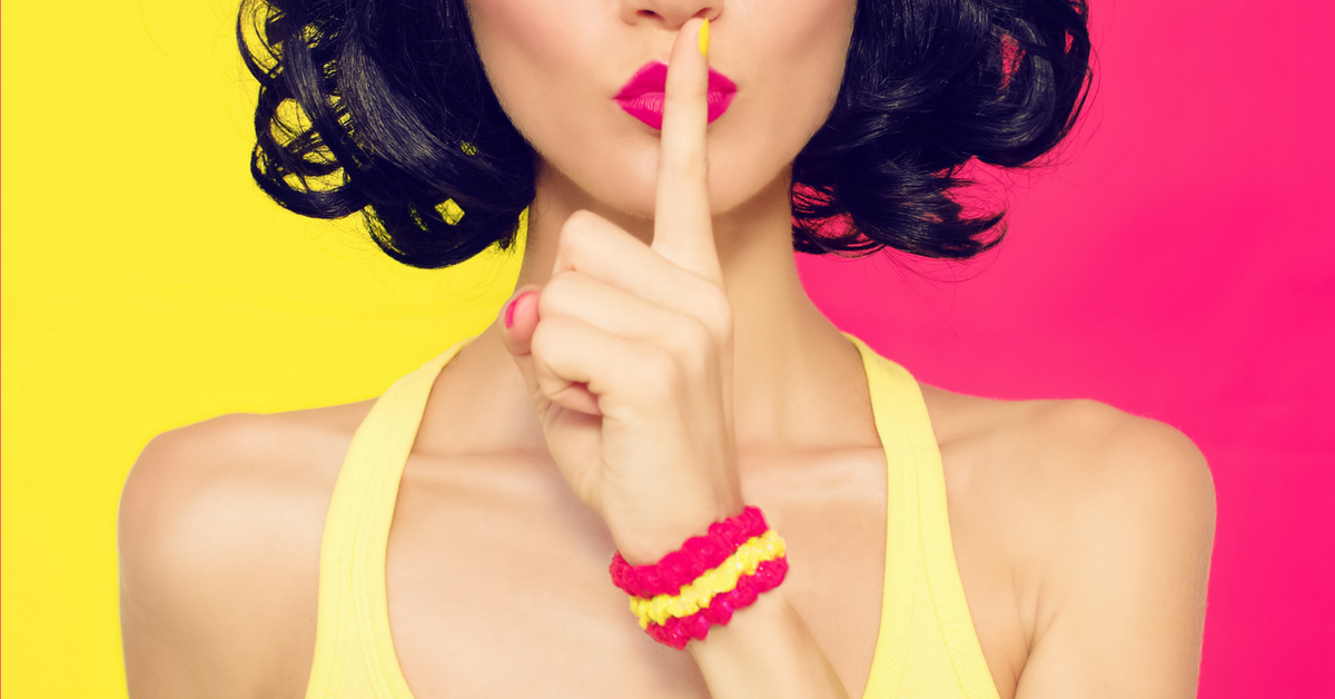 Woman in yellow tanktop, wearing pink and yellow scrunchy on wrist, holding finger up to lips with yellow and pink split background.