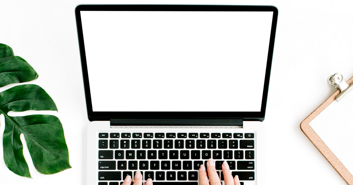 image of a woman typing on a laptop computer on a white desk.