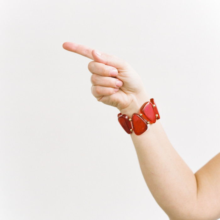 A woman's hand and arm, wearing a red jewel bracelet, pointing to the left.