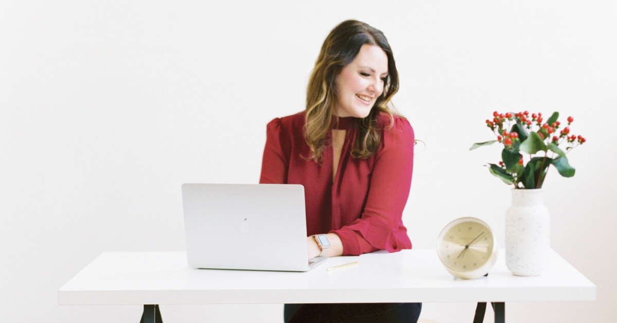 woman sitting at desk smiling typing on laptop. 