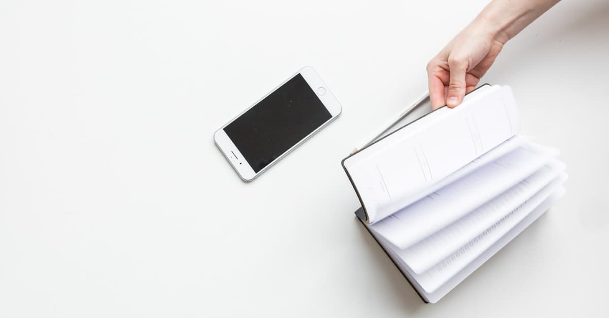 woman flipping through planner with cell phone in reach.