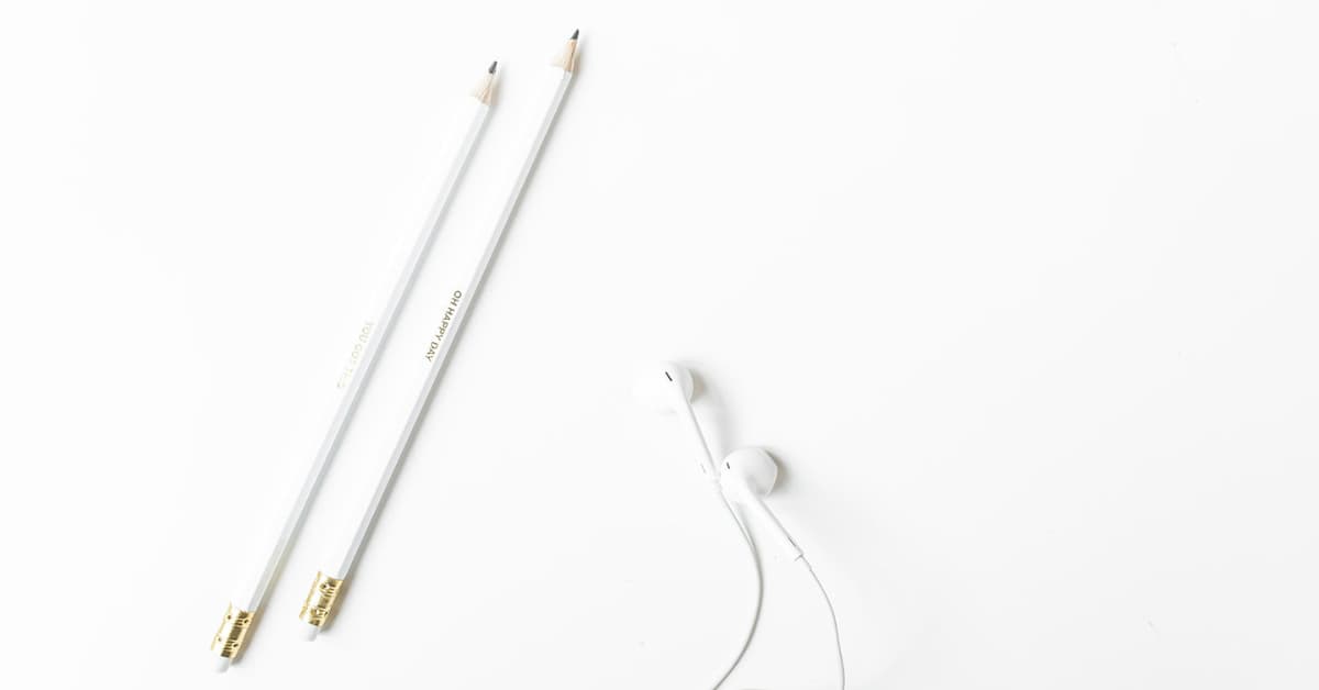 white desk with earbuds and white pencils.