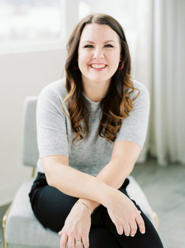 Headshot of Kate Ahl - Simple Pin Media CEO and Founder. Kate is wearing a gray shirt and black pants, has long brown hair, and is smiling at the camera.