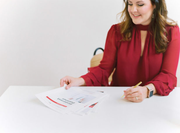 woman wearing red blouse sitting at desk looking at a Pinterest planner.
