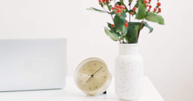 office desk with clock and vase full of flowers.