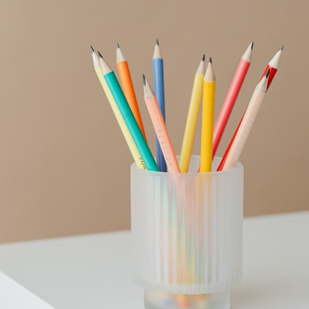 frosted glass cup filled with colored pencils on white table.