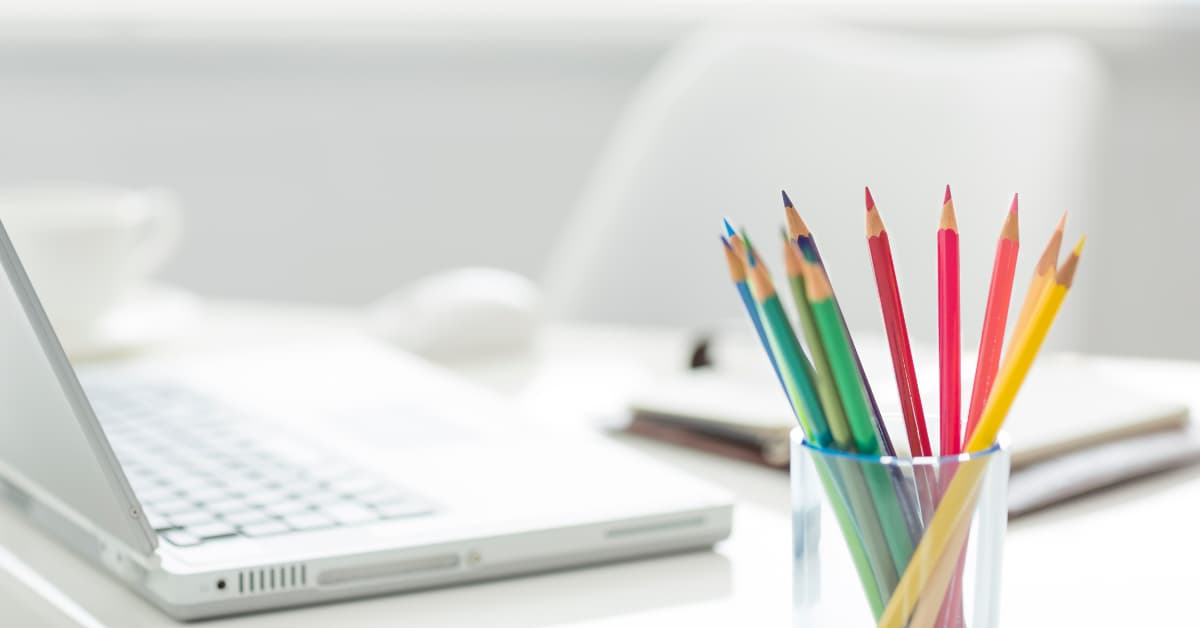 clear glass filled with colored pencils sitting next to white laptop.