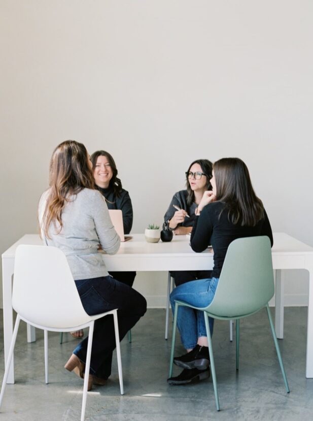 4 women sitting around table talking.
