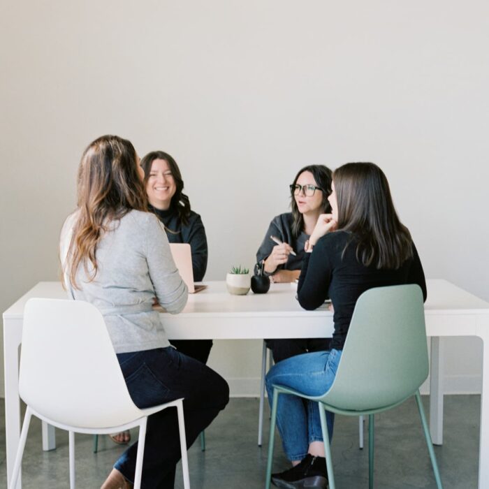 4 women sitting around table talking.
