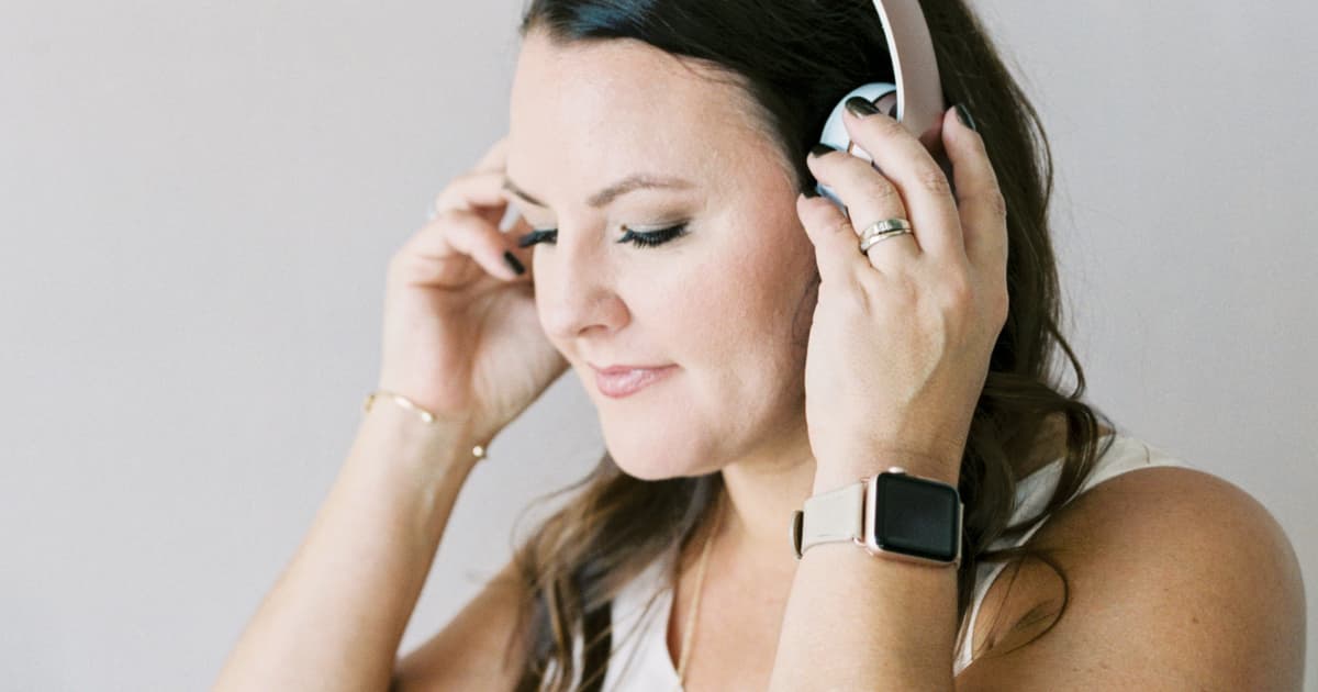 upclose of a woman holding headphones to her ears listening to podcast.