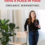 Woman standing behind a chair holding a pair of glasses and smiling. The words "Do Pinterest Ads Have A Place In Your Organic Marketing" are above.