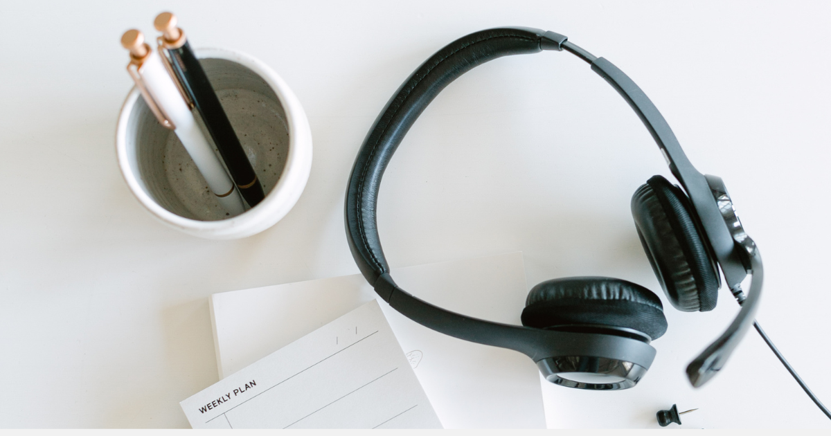 A pair of headphones, a small notebook, and a glass with two pencils in it.