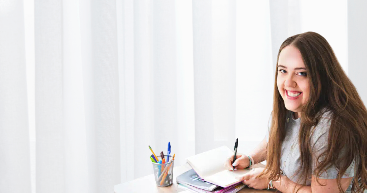 A woman smiling with a pen and paper in hand.