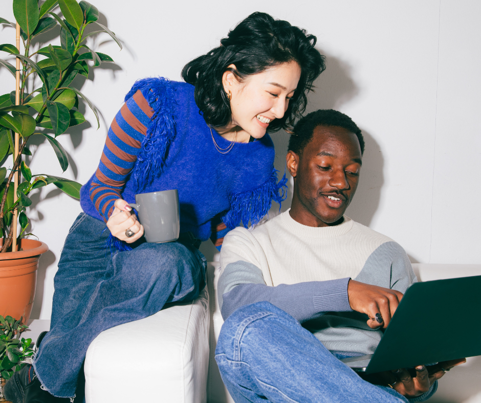 Woman leaning over a man's shoulder as he shares his laptop screen.