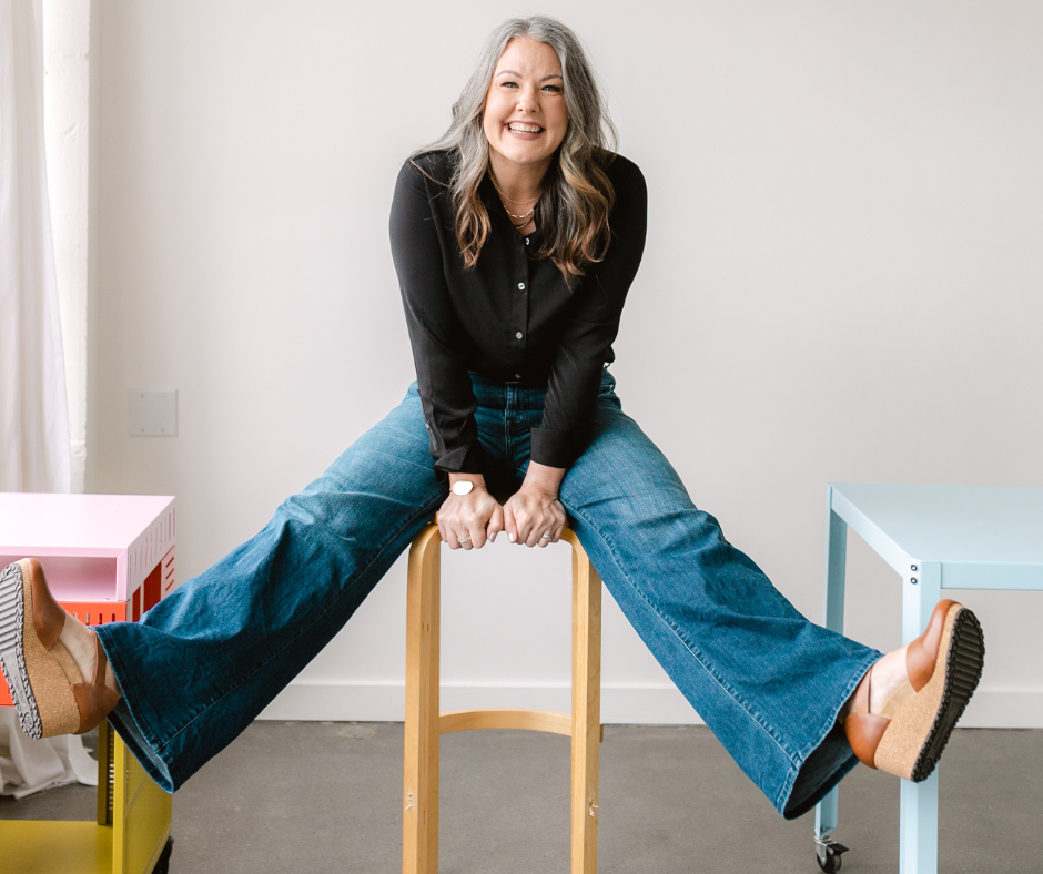 Image shows a woman sitting on a stool smiling.